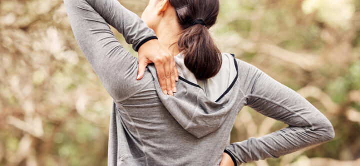 Rearview shot of a woman experiencing back pain while working ou Rearview shot of a woman experiencing back pain while working out in nature.